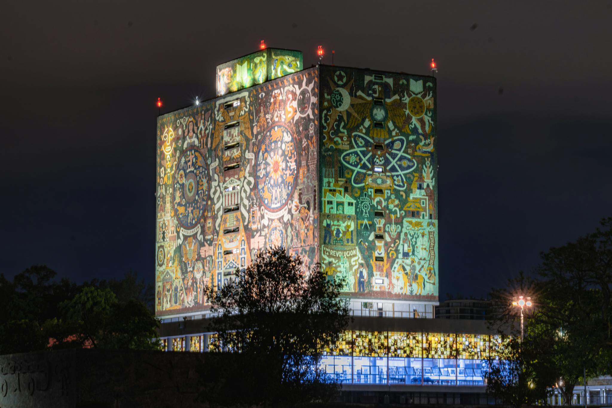 Night view of an illuminated building with a vibrant mural in Mexico City.