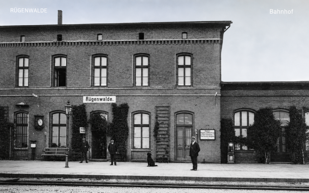 Darłowo (Rügenwalde). Dwukondygnacyjny, ceglany budynek dworca kolejowego obrośnięty winobluszczem, z widocznym personelem i zegarem peronowym. Przełom XIX w. i XX wieku. Karta pocztowa ze zbiorów autora.